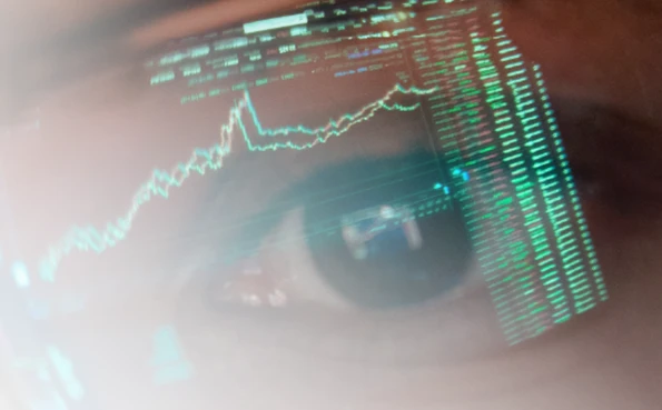 Close-up of a human eye with a reflection of digital charts and code strings, symbolizing constant monitoring in cybersecurity.