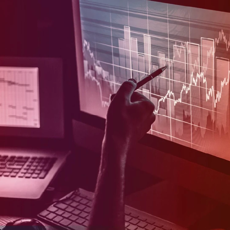 Una mano che tiene una penna indica un grafico a barre e a linee su uno schermo di pc.