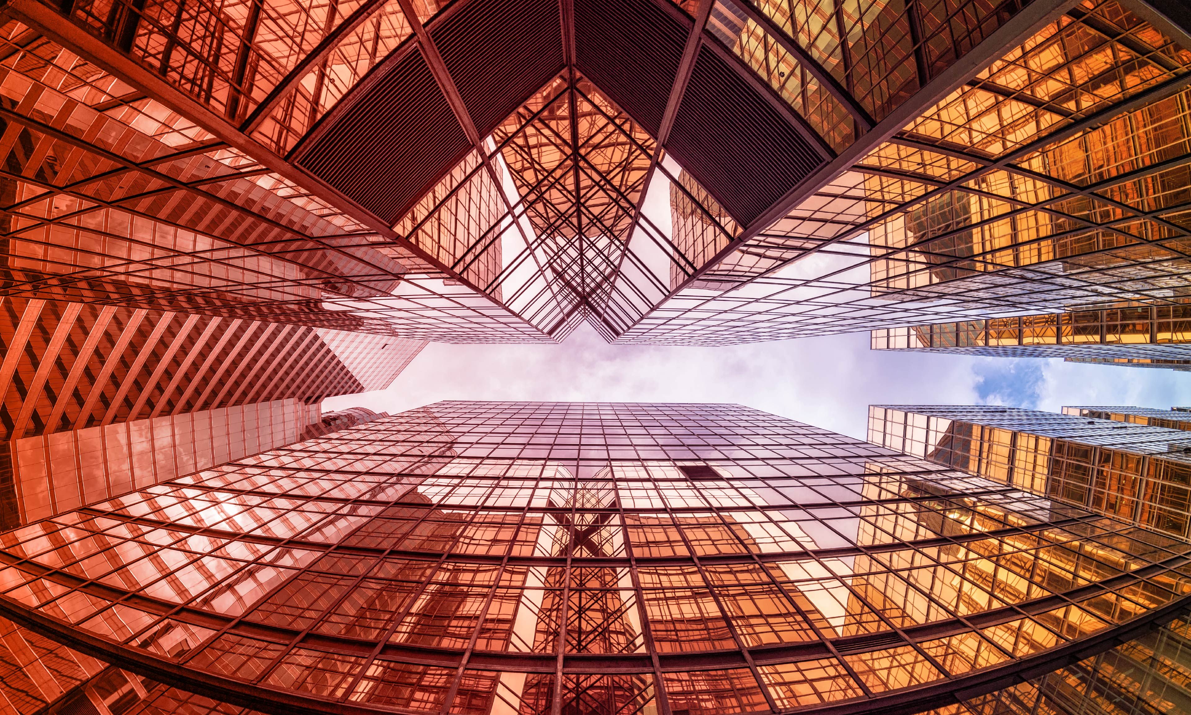 View from below of imposing manufacturing skyscrapers with glass facades and geometric structures.